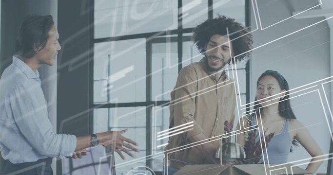 Gesturing man in light blue shirt explaining at office, colleagues unpacking box holding glass vase