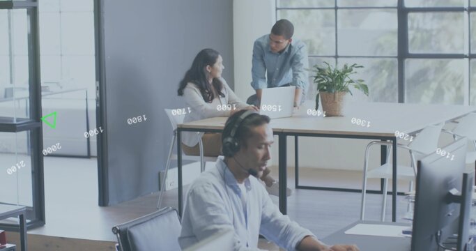 Typing man wearing over-ear headset and button-down shirt at open-plan office, with dual monitors - Powered by Adobe