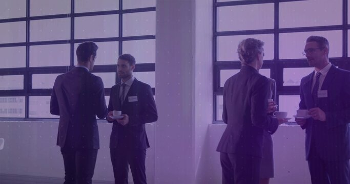 Holding white cups, group wearing suits networking near grid windows with name badges