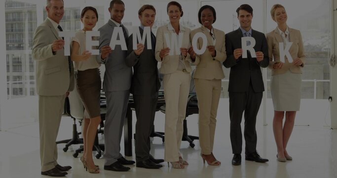 Holding office team wearing suits standing by glass walls near table, displaying letters TEAMWORK