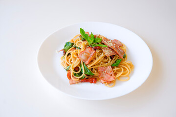 Spicy Spaghetti stir fried with bacon, dried chili and basil on white plate. Thai fusion Italian food style. Isolated on white background