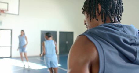 Observing male player wearing sleeveless blue hoodie on gym court, with team in light-blue jerseys