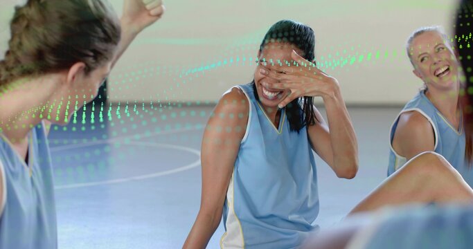 Laughing team sitting on white-lined gym court, woman hiding face in light-blue tops, green overlay