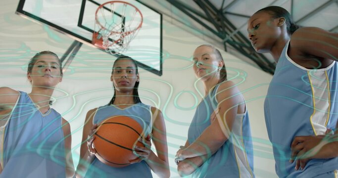 Standing four players wearing light-blue jerseys in gym, holding orange ball beneath hoop