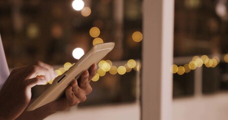 Tapping adult hands with light sleeve cuff using white tablet screen near glass door, string lights © vectorfusionart