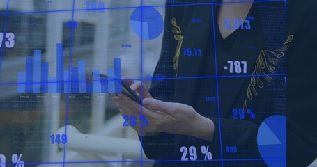 Holding smartphone, woman in dark blazer with gold trim viewing blue data charts at office