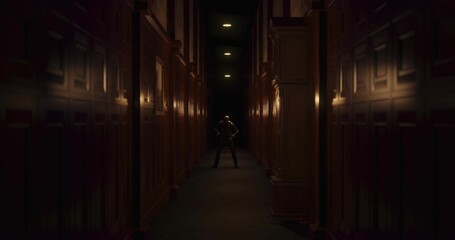 Standing man in dark suit in dim wood-paneled corridor with pilasters, recessed lights, carpet