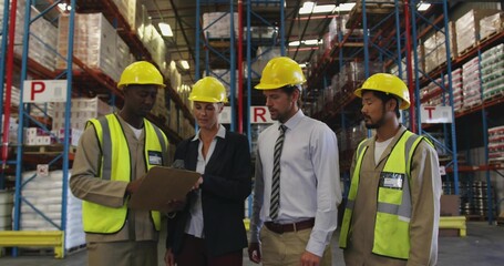 Inspecting team of four checking clipboard in warehouse aisle, wearing hard hats hivis vests jacket