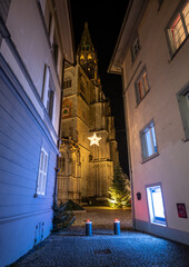 Illuminated cathedral “Münster unserer lieben Frau” (Cathedral of Our Lady), photographed from an alley at night. Konstanz, Baden-Württemberg, Germany.