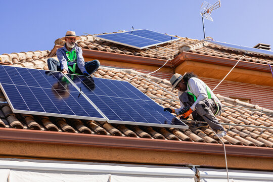 Workers installing solar panels on house roof - Powered by Adobe