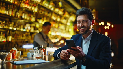 Cheerful guy looking smartphone in pub closeup. Smiling man messaging friends