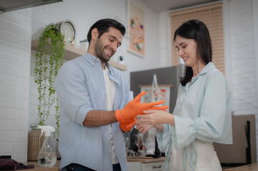 Fototapeta premium Couple preparing to clean kitchen, helping each other put on gloves.