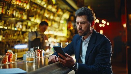 Depressed man looking cellphone screen at night pub. Sad guy feeling stress