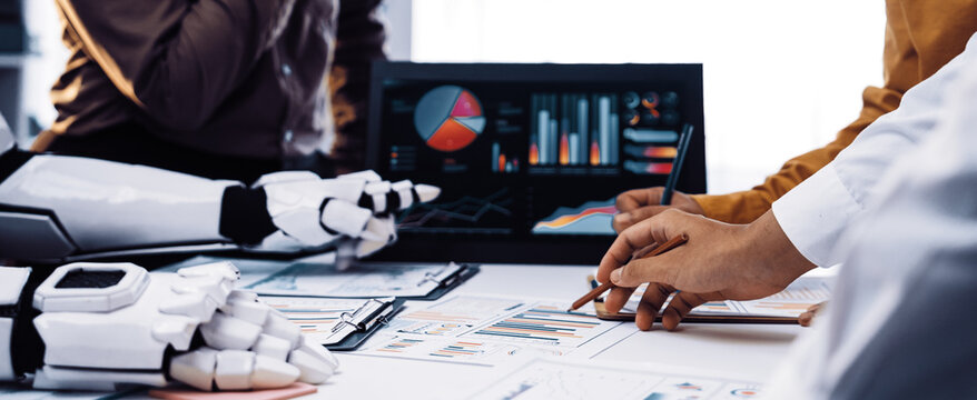 Humans and robots collaborate in a modern workspace, analyzing data charts and graphs. The image captures the essence of technology integration in decision-making processes.Noogenesis - Powered by Adobe