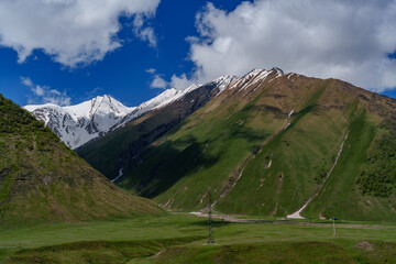 Fototapeta premium Snowy Caucasus ridges above smooth green valley with power masts