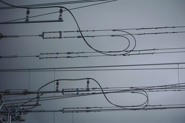 Power lines stretch across a cloudy sky in an industrial area, highlighting the intricate design and symmetry of electrical infrastructure