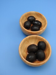 Set of black olives in wooden elements on a blue background