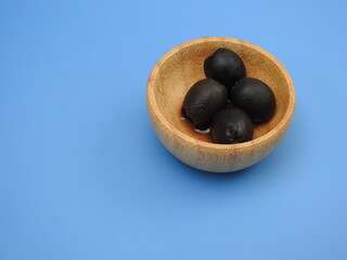 Set of black olives in wooden elements on a blue background