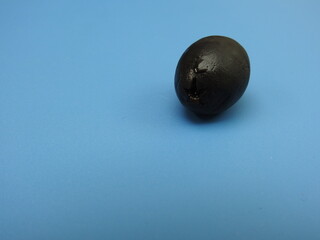 A solitary black olive placed on a blue background