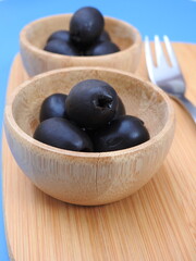 Set of black olives in wooden elements on a blue background