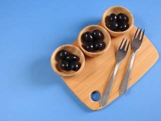 Set of black olives in wooden elements on a blue background