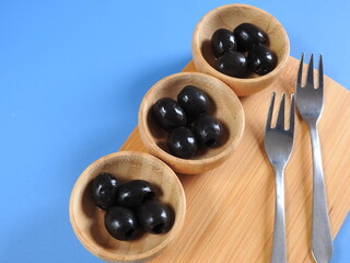 Set of black olives in wooden elements on a blue background