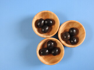 Set of black olives in wooden elements on a blue background