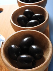 Set of black olives in wooden elements on a blue background