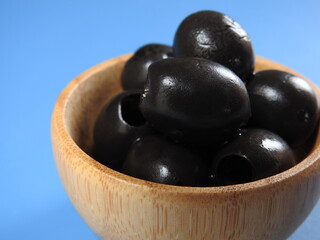 Set of black olives in wooden elements on a blue background