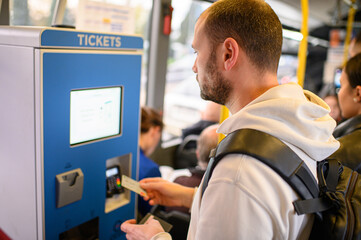 Man buying a bus ticket at a ticket machine. Urban transportation, public transit, everyday life, commuting, city lifestyle, and independent travel. © Mariia Andreeva