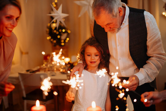 Grandparents and granddaughter holding sparklers during Christmas celebration.