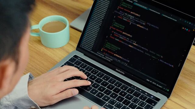 Programmer Writing Code on Laptop Computer with Coffee Cup at Wooden Desk Workspace