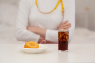 Woman on diet refusing soda and donut with hand gesture, symbolizing healthy lifestyle, sugar reduction, calorie control, and commitment to clean eating for weight loss.