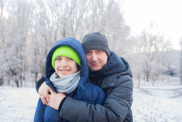 Fototapeta premium A father hugs his teenage son, the boy and his dad pose for a photo in a winter snowy park