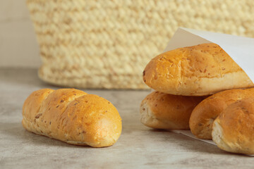 Five loaves of small French baguette bread on the countertop. Tiny fresh sandwich bread wrapped in paper on a gray surface.