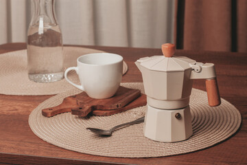 Coffee preparation on a wooden table with a stylish moka pot and a white cup