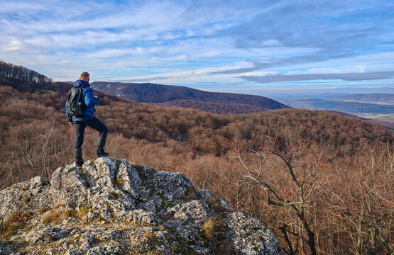 A hiker stands on a rocky outcrop and looks across the rolling hills and winter forests of the Bükk Mountains. Peaceful outdoor adventure scene with expansive mountain views.