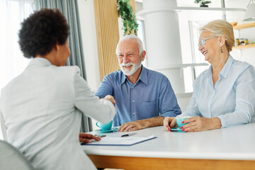 Obraz premium Portrait of a businesswoman or real estate agent or doctor shaking hands and signing a deal contract with senior couple in his office