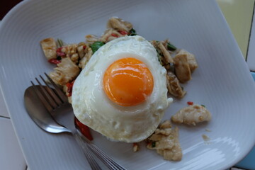 The classic Thai dish, Pad Krapow Gai (Stir-fried Chicken with Holy Basil), features succulent pieces of chicken stir-fried with fiery chili and fragrant basil, crowned dramatically with a perfectly.