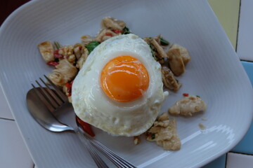 The classic Thai dish, Pad Krapow Gai (Stir-fried Chicken with Holy Basil), features succulent pieces of chicken stir-fried with fiery chili and fragrant basil, crowned dramatically with a perfectly.