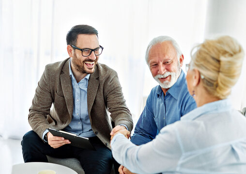 Portrait of a businessman or real estate agent or doctor shaking hands and signing a deal contract with senior couple in his office