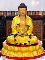 Golden Buddha statue resting on a red and gold lotus pedestal in a temple hall at Kek Lok Si, Penang, Malaysia. The figure is depicted in a traditional meditative pose.