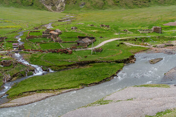 Waterfalls and hamlet above eroded riverbank in remote mountain valley