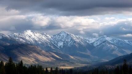 Majestic snow capped mountain range beneath dramatic stormy clouds with golden light illuminating the valley below