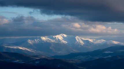 Majestic snow capped mountain range under dramatic stormy clouds during golden hour