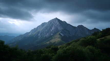 Fototapeta premium Dramatic mountain peak under stormy cloudy skies at dusk with lush green foreground