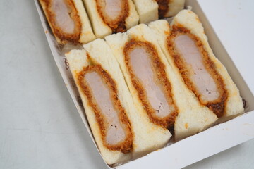 肉厚なとんかつを挟んだカツサンドのボックス入り俯瞰写真。ジューシーな断面と衣のサクサク感が食欲を引き立てる。テイクアウト・ランチ素材・食レポ記事・飲食店広告にも使いやすい高品質な料理イメージ