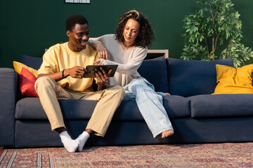 Diverse couple relaxing on couch using digital tablet