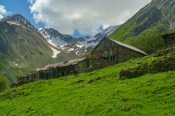 Old mountain farmstead on green slope beneath snowy Caucasus ridges