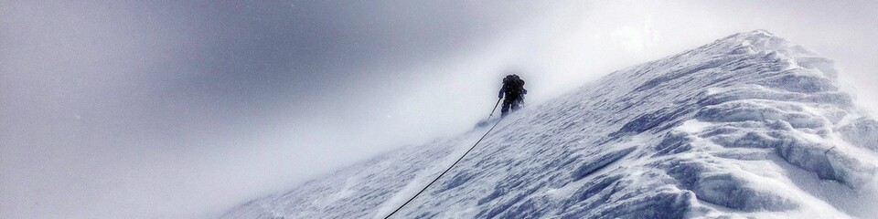 Obraz premium Climber trekking icy mountain ridge through dense fog. Solo mountaineer navigating a challenging snowy ridge against a foggy sky